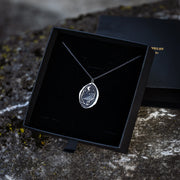 a silver necklace depicting a raven and crescent moon with wax seal styling in a black gift box