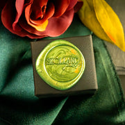 Black ring box that features 'Skolland' branding on a green wax seal with flowers in the background