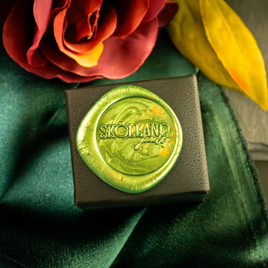 Black ring box that features 'Skolland' branding on a green wax seal with flowers in the background