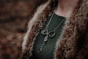 A symbolic,uterus shaped necklace is worn on a womans chest. The base of the neckalce is a bezel set, red dravite tourmaline