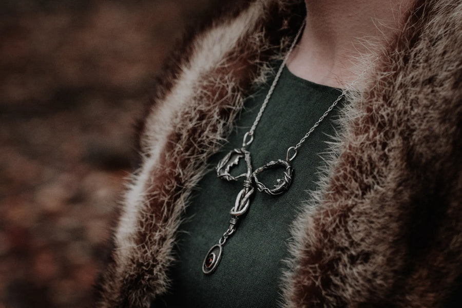 A symbolic,uterus shaped necklace is worn on a womans chest. The base of the neckalce is a bezel set, red dravite tourmaline