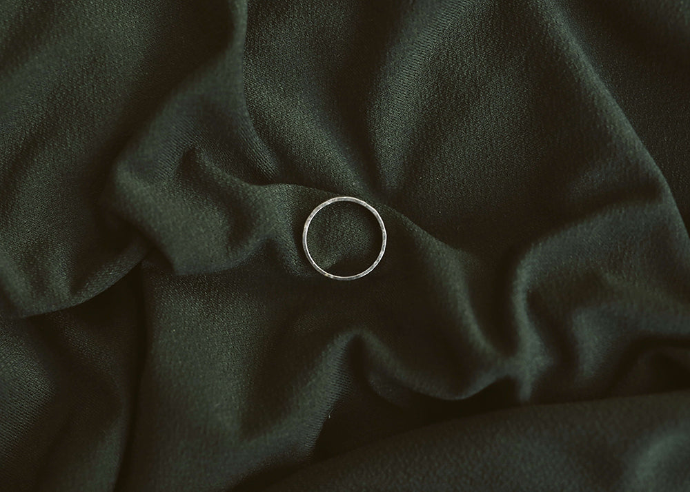A silver ring rests on a dark green fabric, creating a subtle contrast. The material is softly gathered, adding an elegant, serene ambiance.