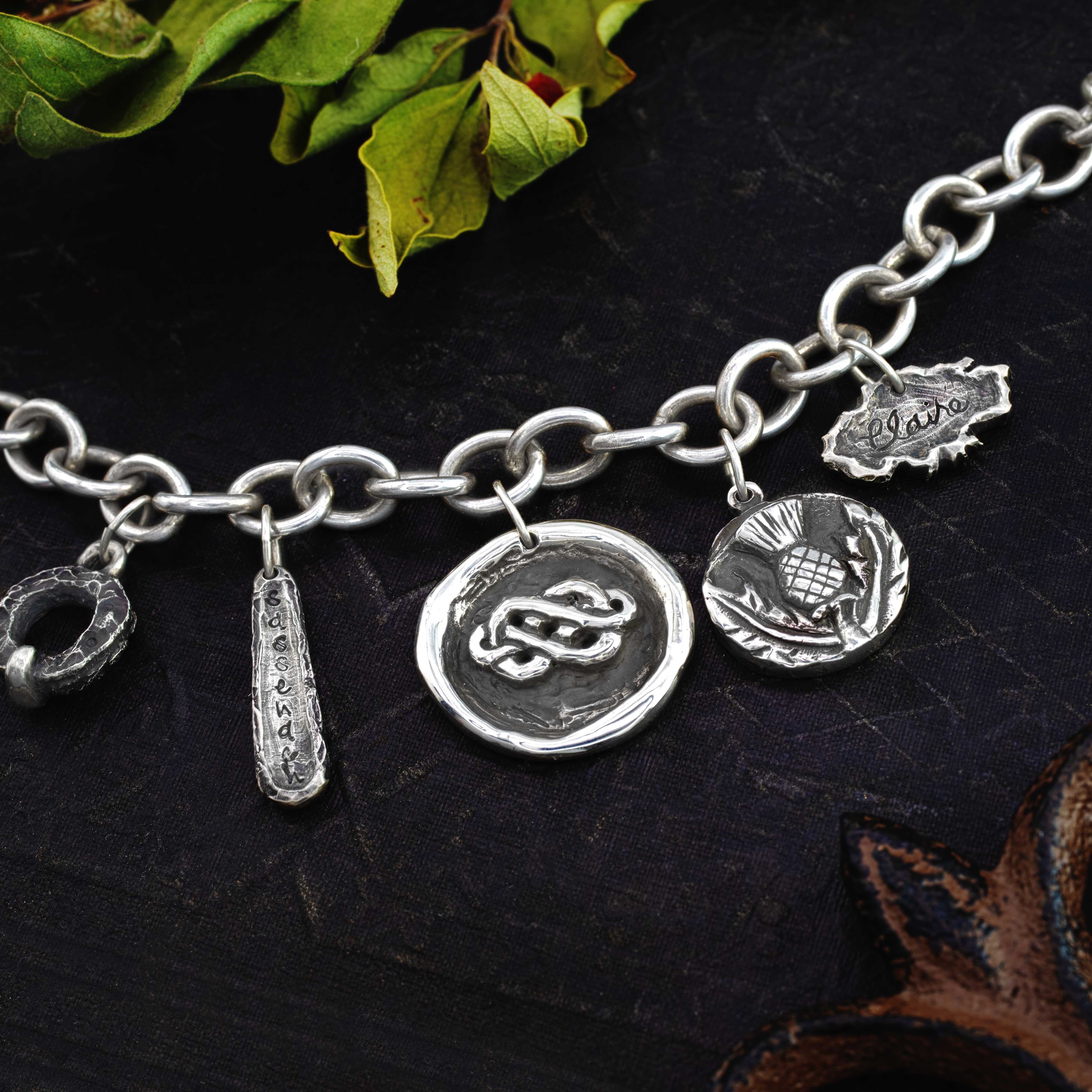 hand crafted silver charms on a sterling silver charm bracelet, the charms feature thistle designs, celtic knots, historical, and  ripped parchment styling