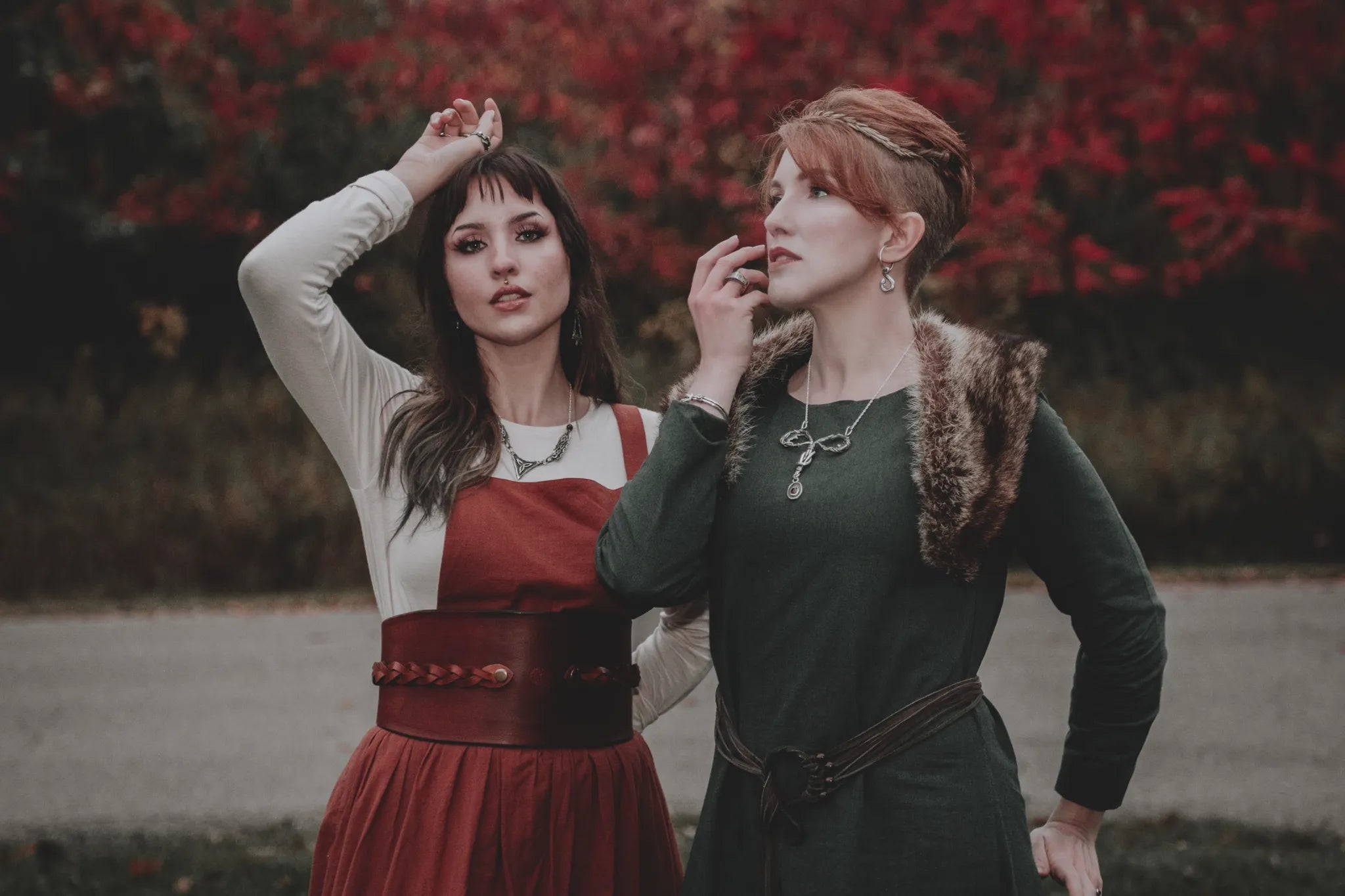2 women wearing bold,celtic jewelry pose in a forest. They are wearing, necklaces,earrings,bracelets and rings.