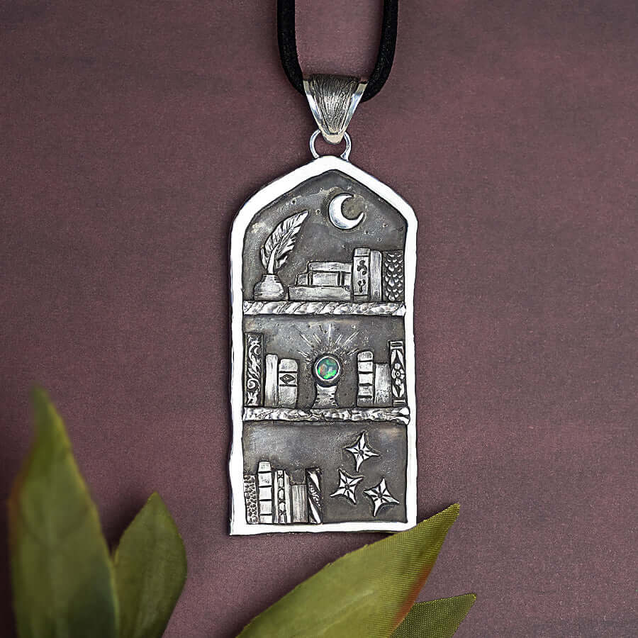 Etched silver charm featuring a bookcase filled with books and glowing orb