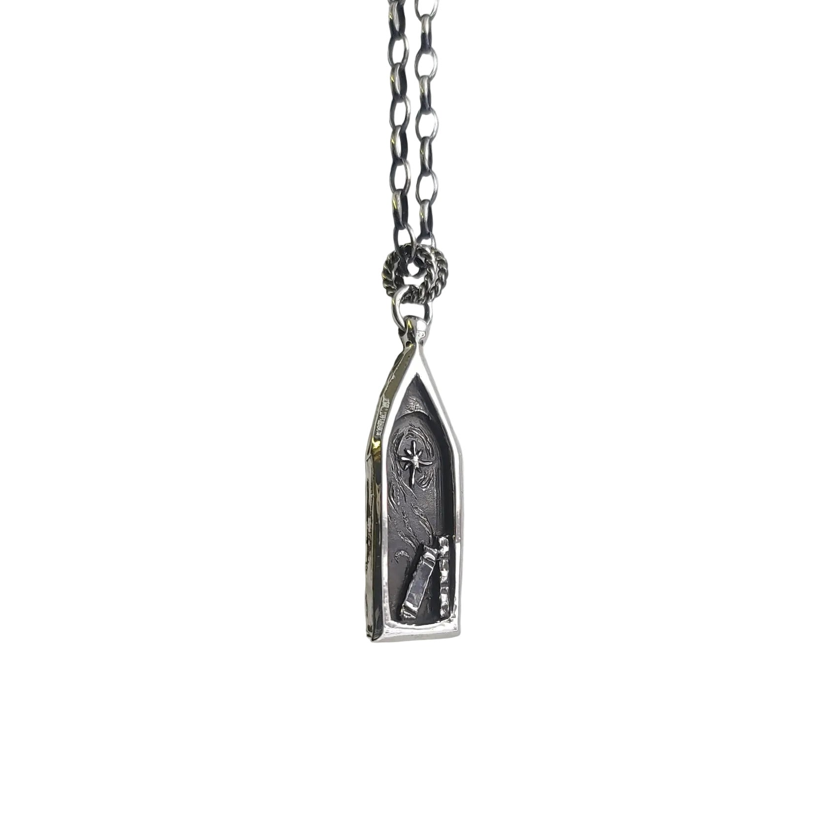 An artisan made silver necklace featuring a gothic style window, a north star, and books. The artist has named this piece "A light in the abbey"