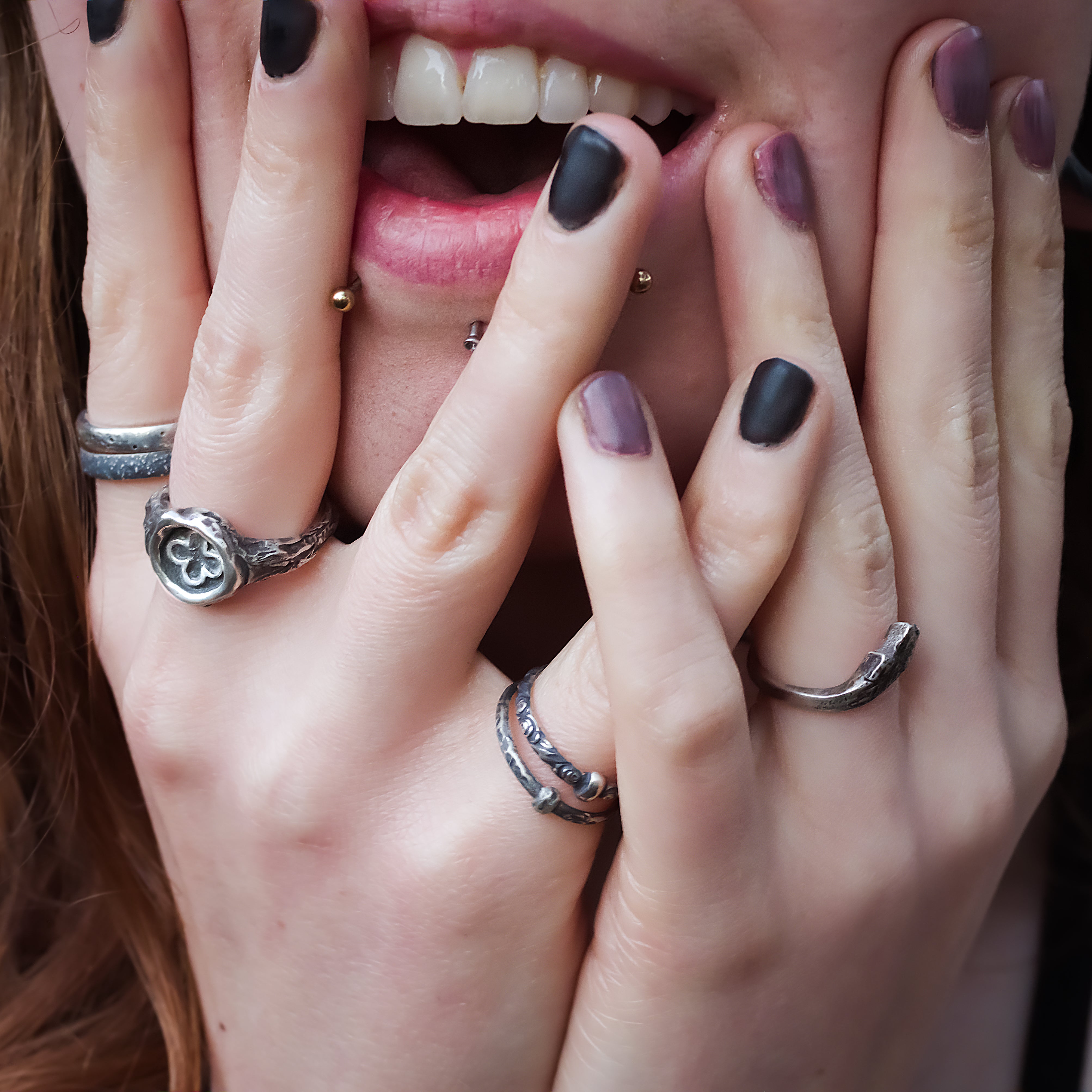 Woman with hands on face while wearing several unique, handmade rings