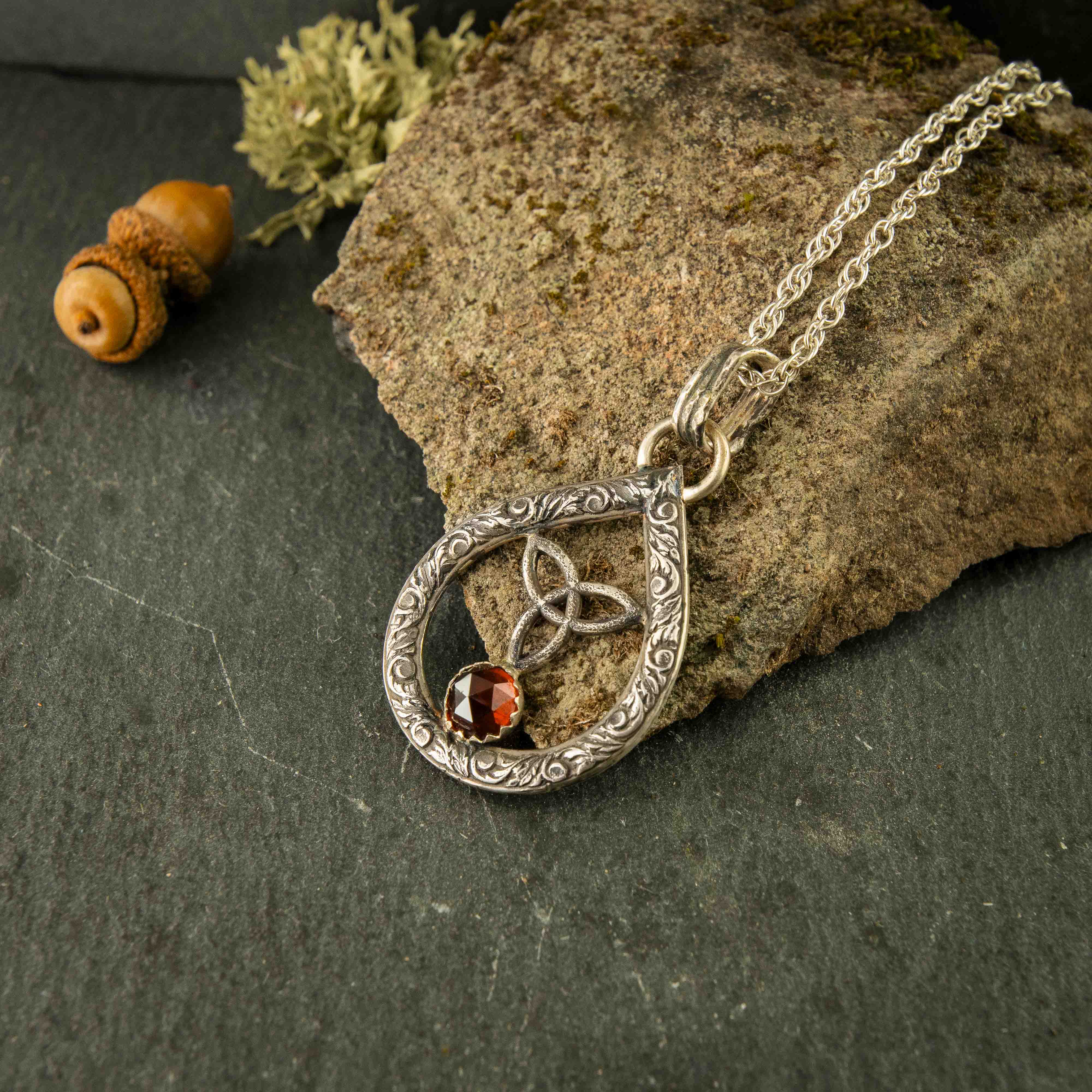 The maiden necklace, a tear dropped shaped sterling silver pendant that freatures a trinity knot, rosecut garnet and filigree styling. Handmade in the USA with ethical craftsmanship