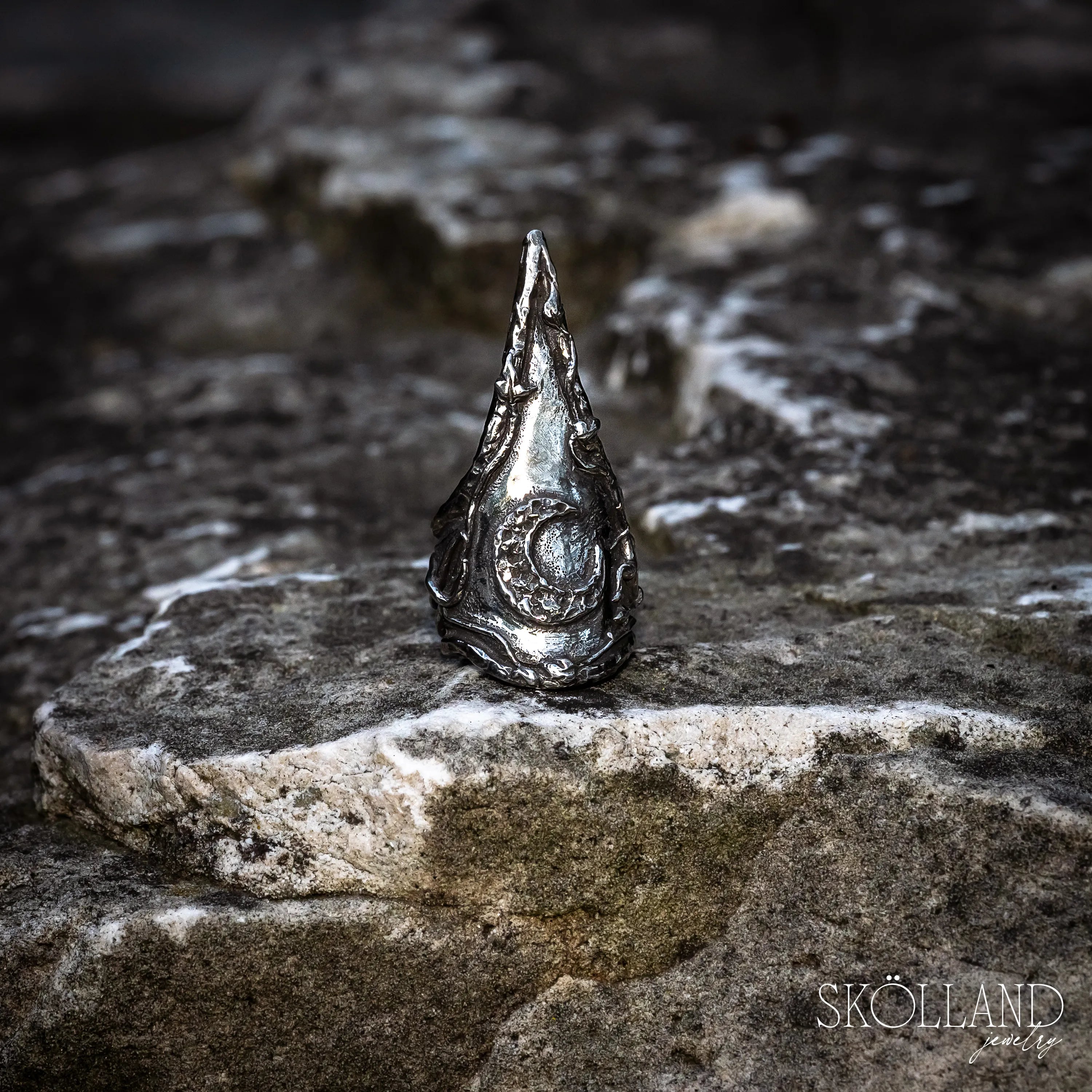 Silver ring with a moon and ivy vine design on a stone surface, branded 'Skölland'.
