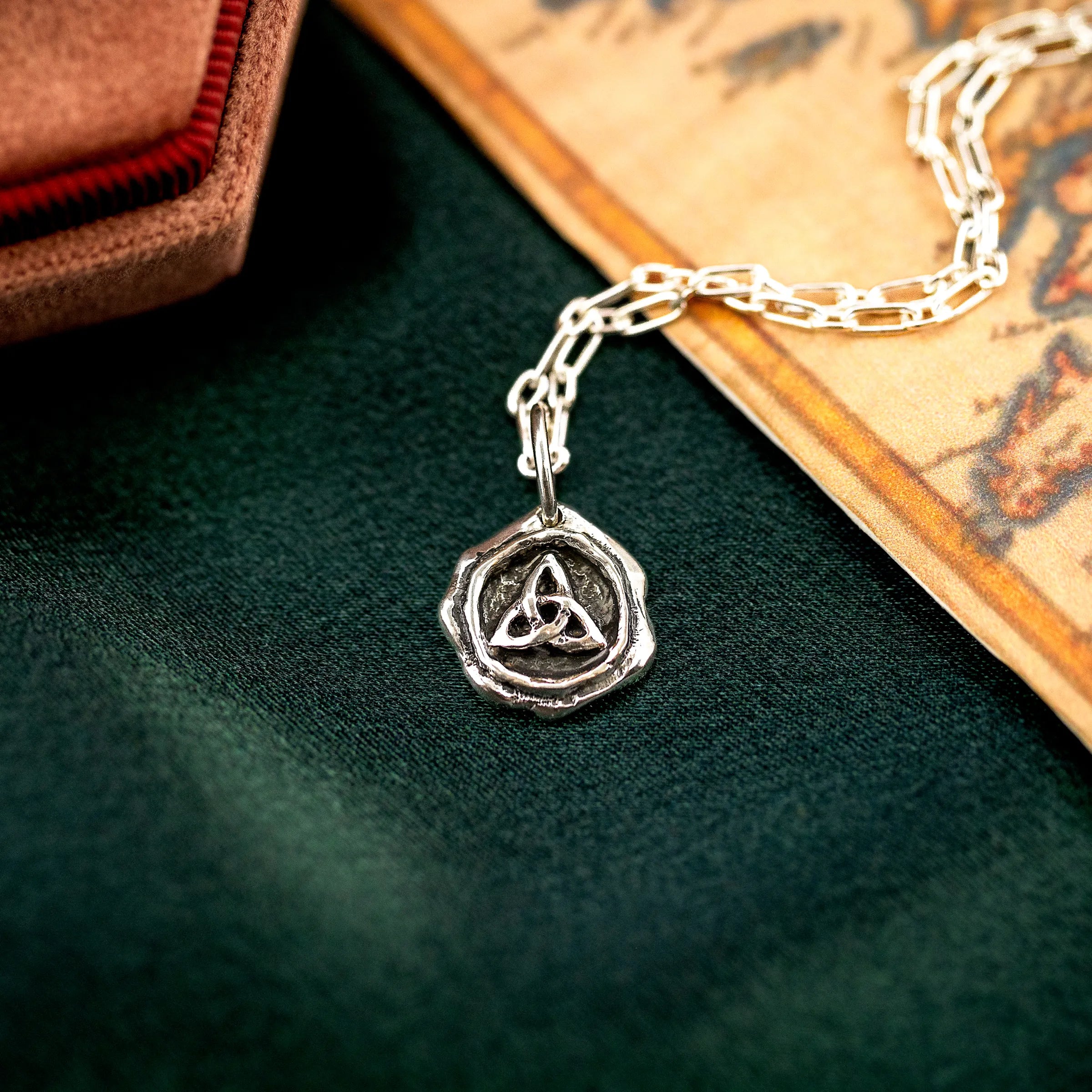 A small trinity knot necklace with wax seal styling. Made from solid sterling silver, displayed on a sterling silver chain