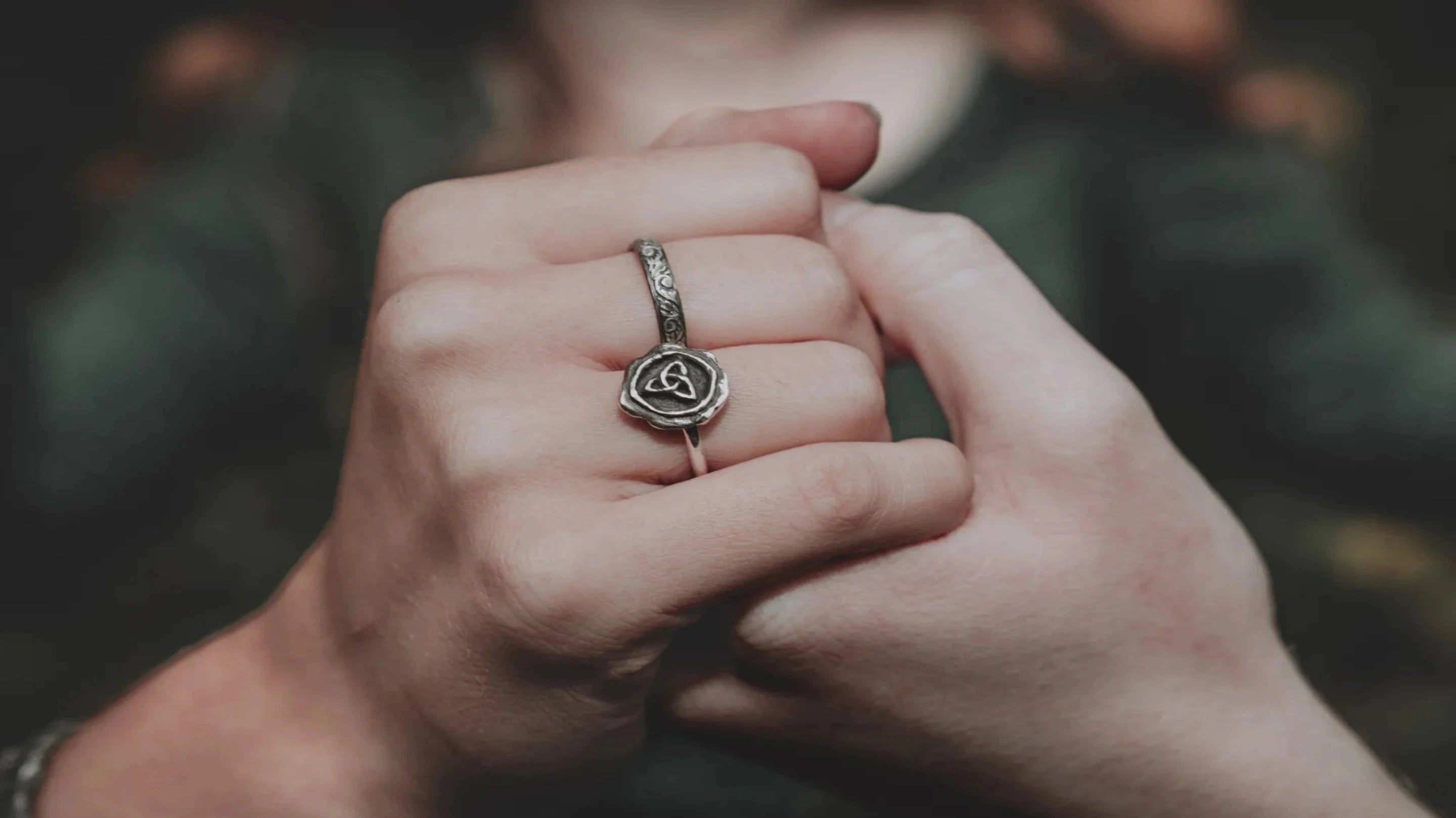 Close-up of a hand wearing a 2 silver rings-a trinity knot ring, and one with a filigree design.