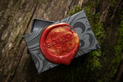 red wax seal that reads "Skolland Jewelry" on a black and gray swirl ring box