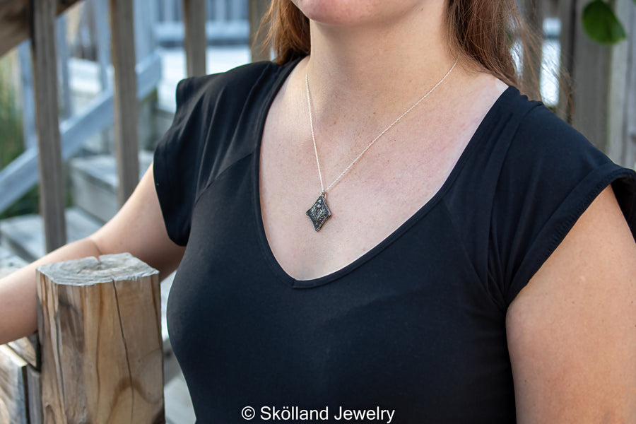 The thistle necklace being worn on a model at an 18 inch chain length. The pendant and necklace are made of sterling silver