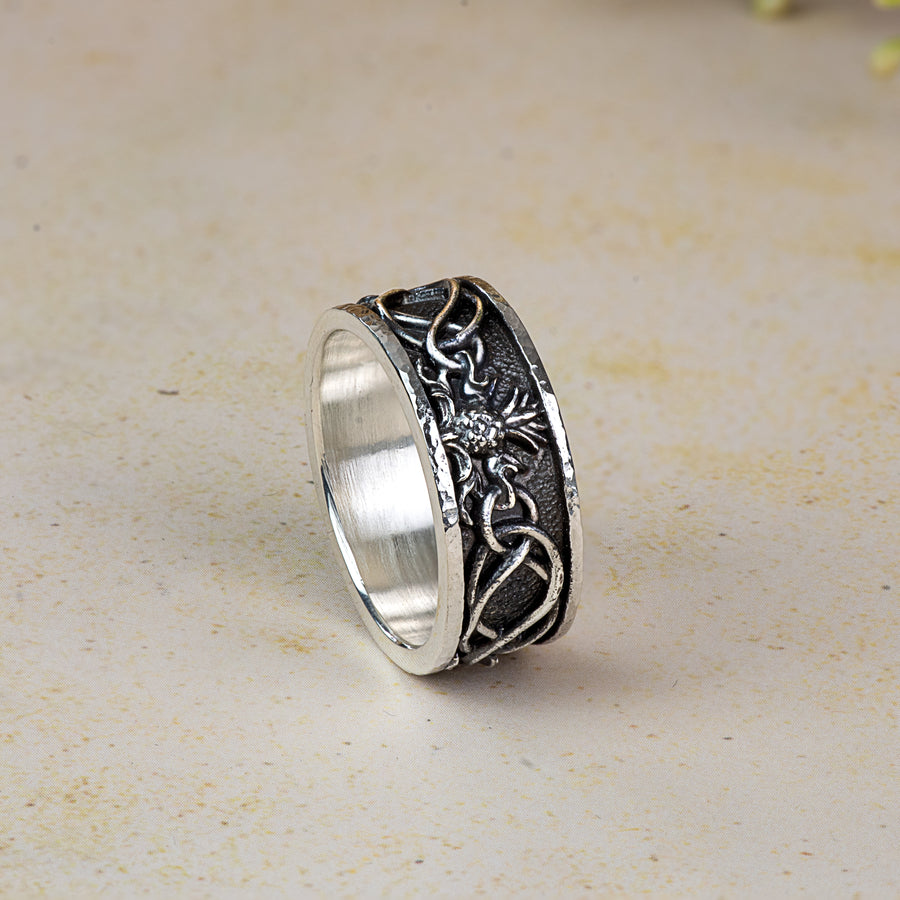 Silver ring with intricate thistle and knot work designs on a beige background