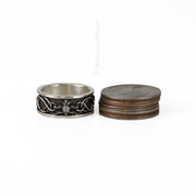 a silver thistle band with knot details next to a stack of 5 US quarters for scale
