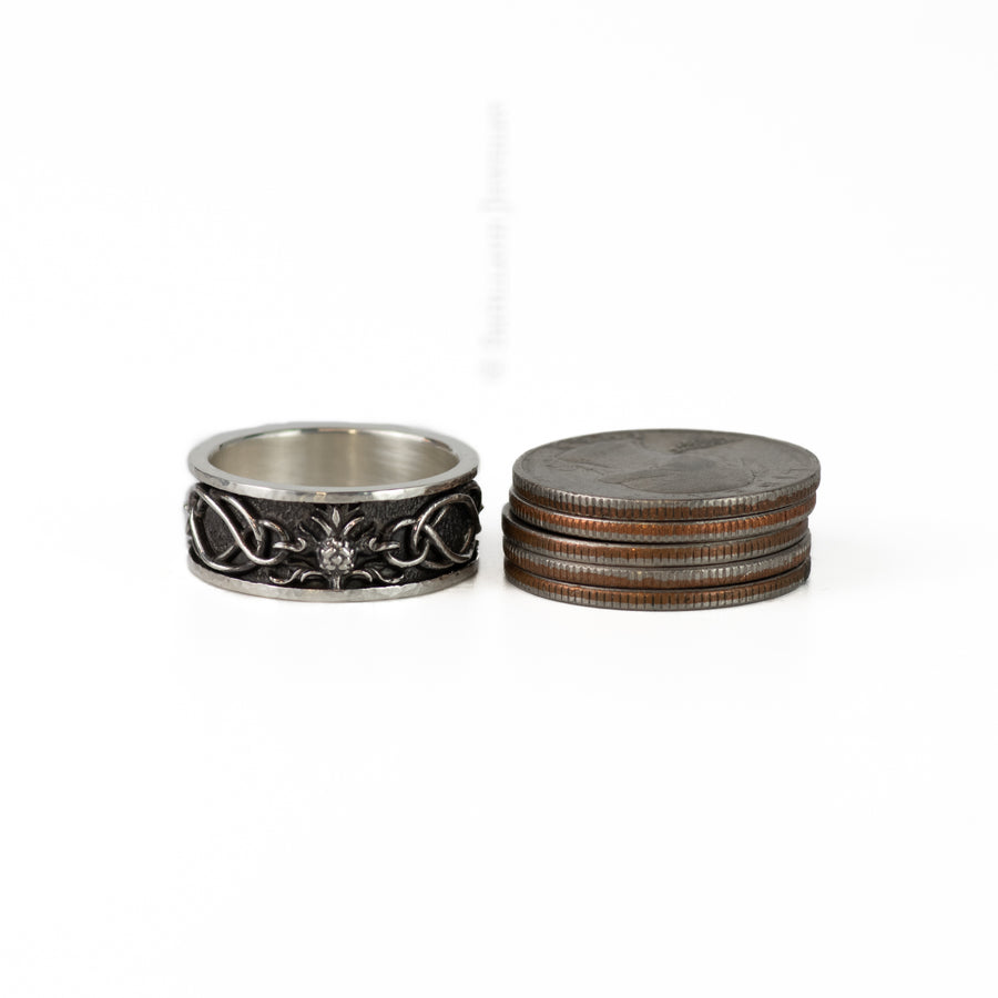 a silver thistle band with knot details next to a stack of 5 US quarters for scale
